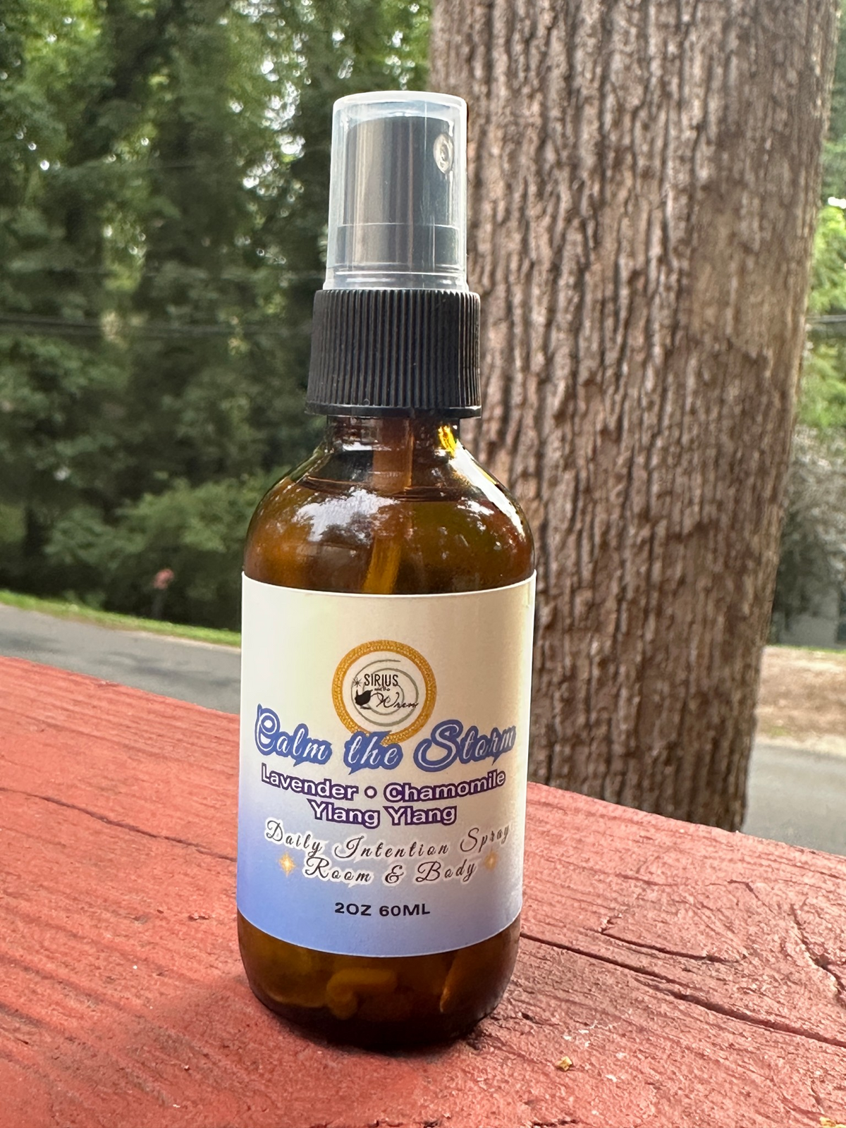 Calm the Storm Daily Intention Spray, 2 oz, on a wooden surface with a tree in the background