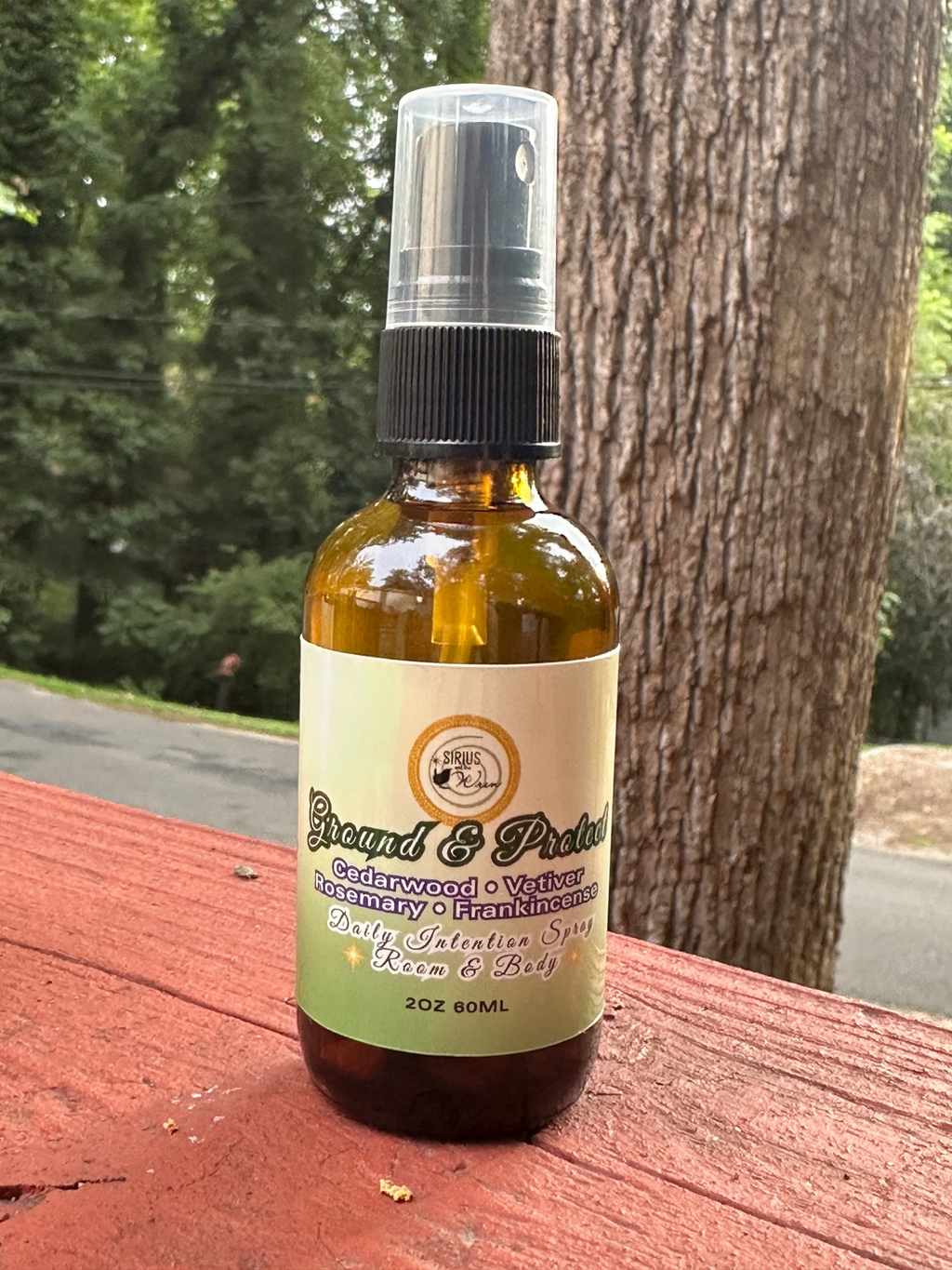 Ground + Protect Daily Intention Spray, 2 oz, on a wooden surface with a tree in the background