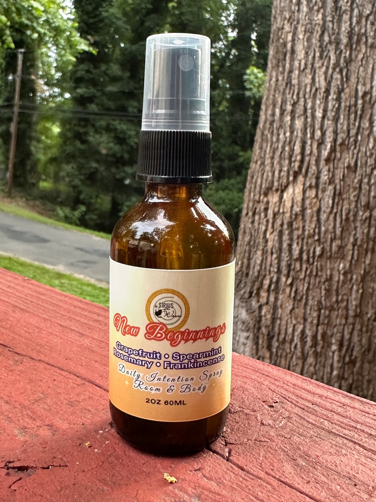 New Beginnings Daily Intention Spray, 2 oz, on a wooden surface with a tree in the background