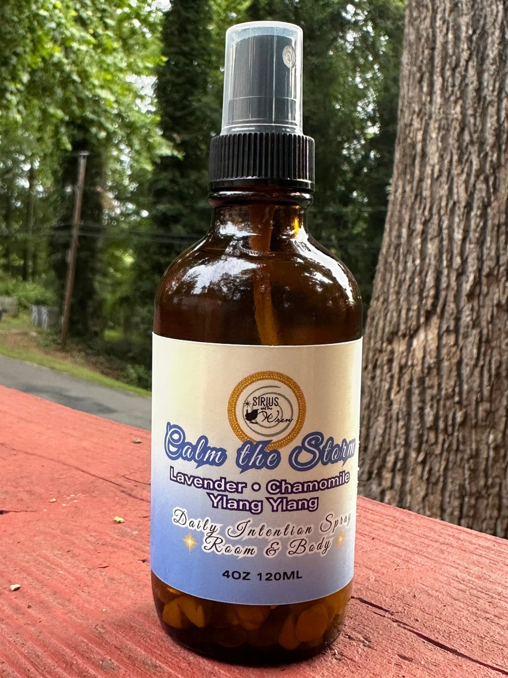 Calm the Storm Daily Intention Spray, 4 oz, on a wooden surface with trees in the background