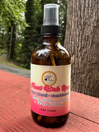 Heart Wide Open Daily Intention Spray, 4 oz, with a pink label on a wooden surface outdoors