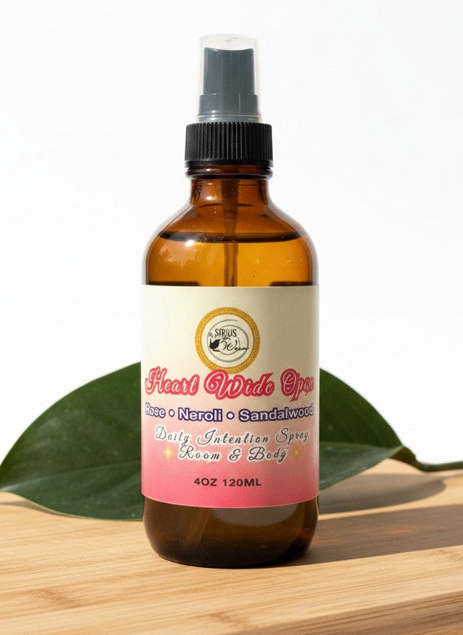 Heart Wide Open Daily Intention Spray, 4 oz, with a pink label on a wooden surface with green leaves