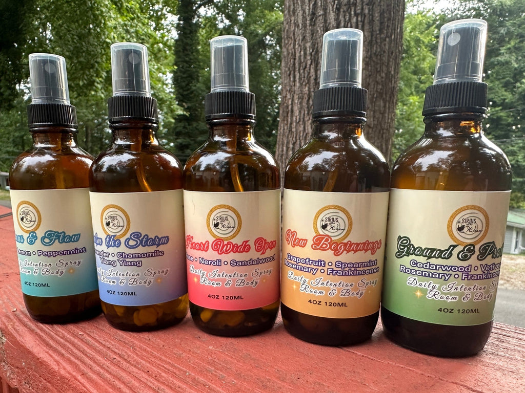 All of the 4 oz Daily Intention Sprays together on a wooden surface with trees and greenery in the background