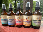 All of the 4 oz Daily Intention Sprays together on a wooden surface with trees and greenery in the background