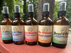 All of the 4 oz Daily Intention Sprays together on a wooden surface with trees and greenery in the background