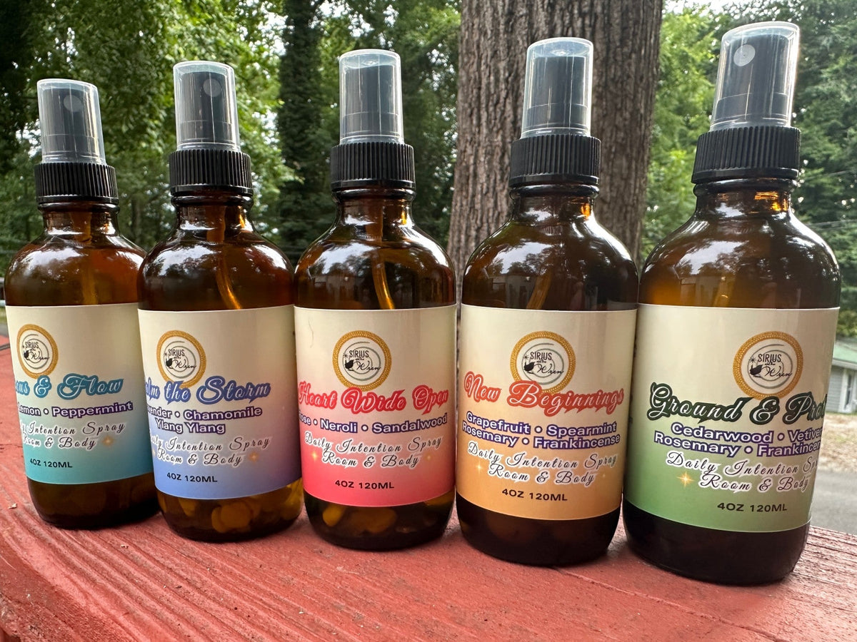 All of the 4 oz Daily Intention Sprays together on a wooden surface with trees and greenery in the background