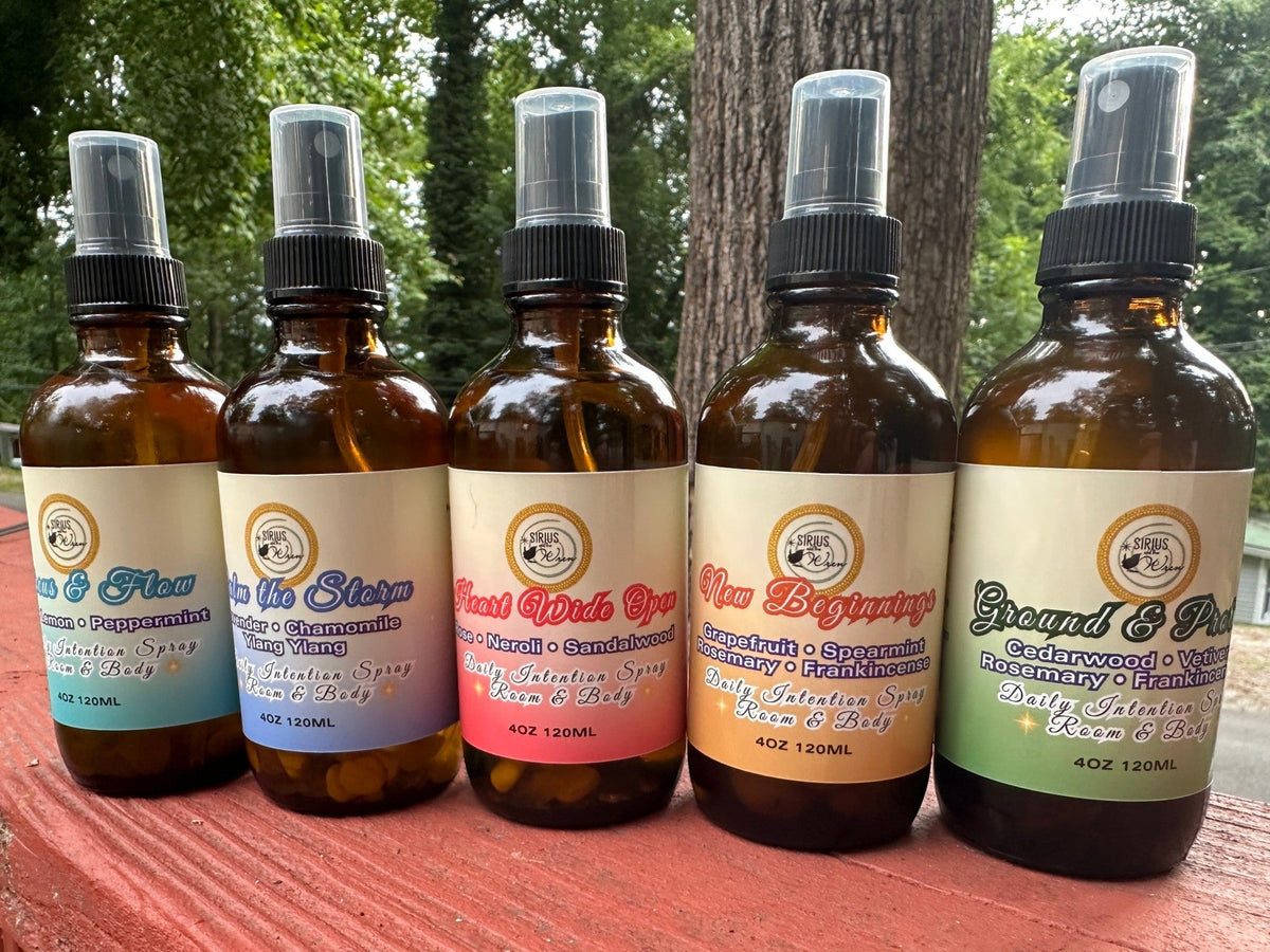 All of the 4 oz Daily Intention Sprays together on a wooden surface with trees and greenery in the background