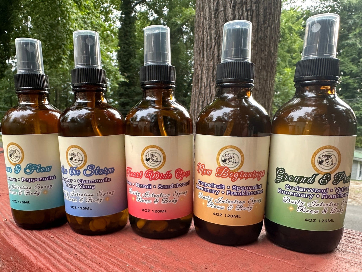 All of the 4 oz Daily Intention Sprays together on a wooden surface with trees and greenery in the background