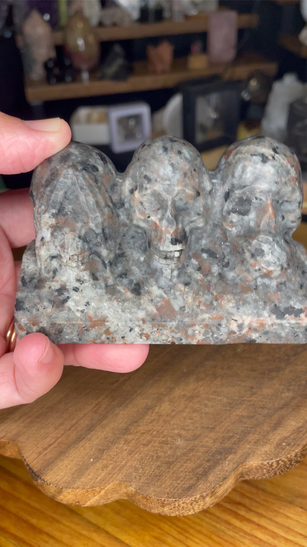 A hand holds a gray and speckled Yooperlite See No Evil, Hear No Evil, Speak No Evil Carving - 402 g, which features three skulls representing see no evil, hear no evil, and speak no evil.