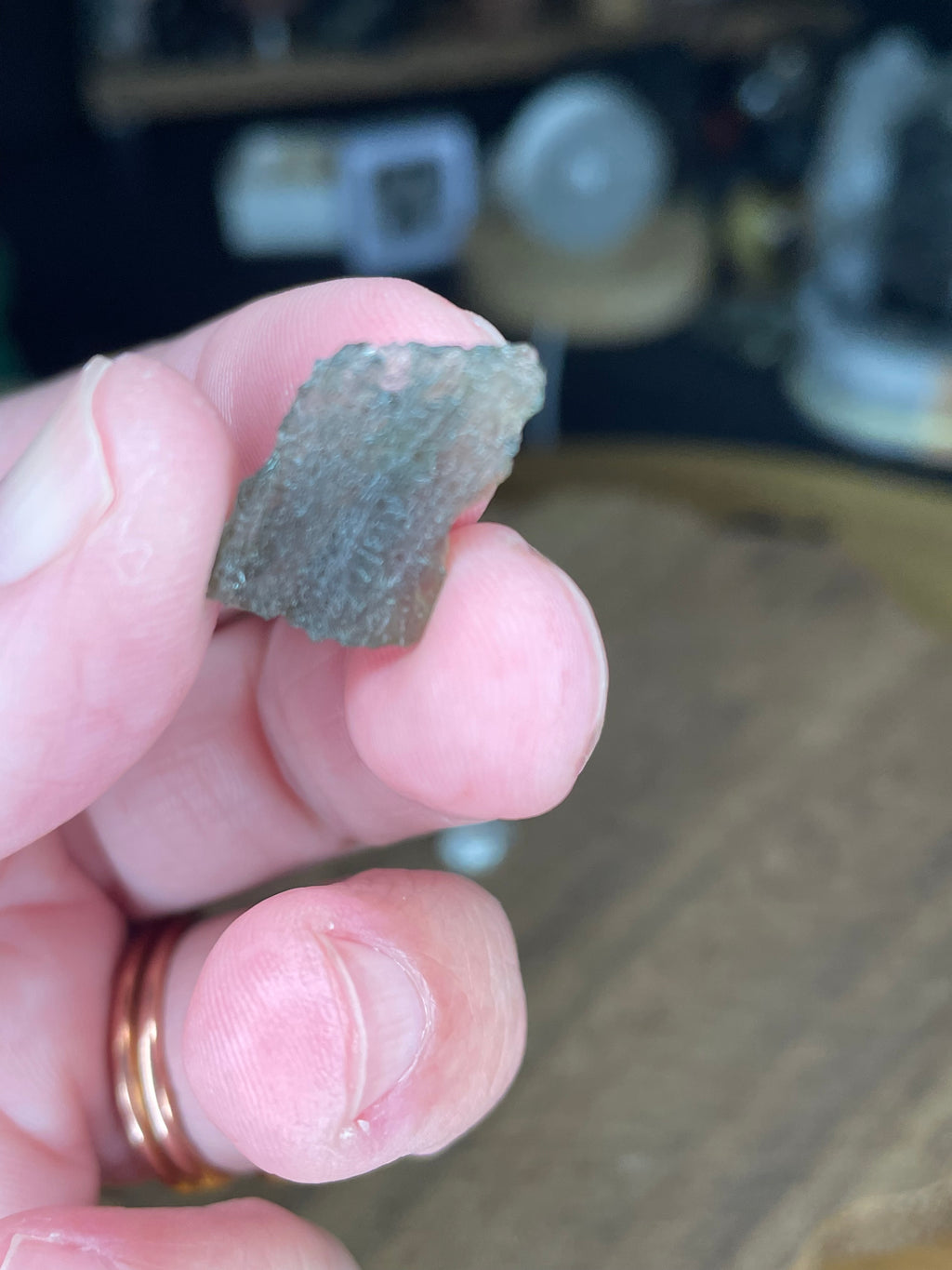 A hand holding a small, textured, translucent green Moldavite with Herkimer Diamonds - 1.15 g fragment.