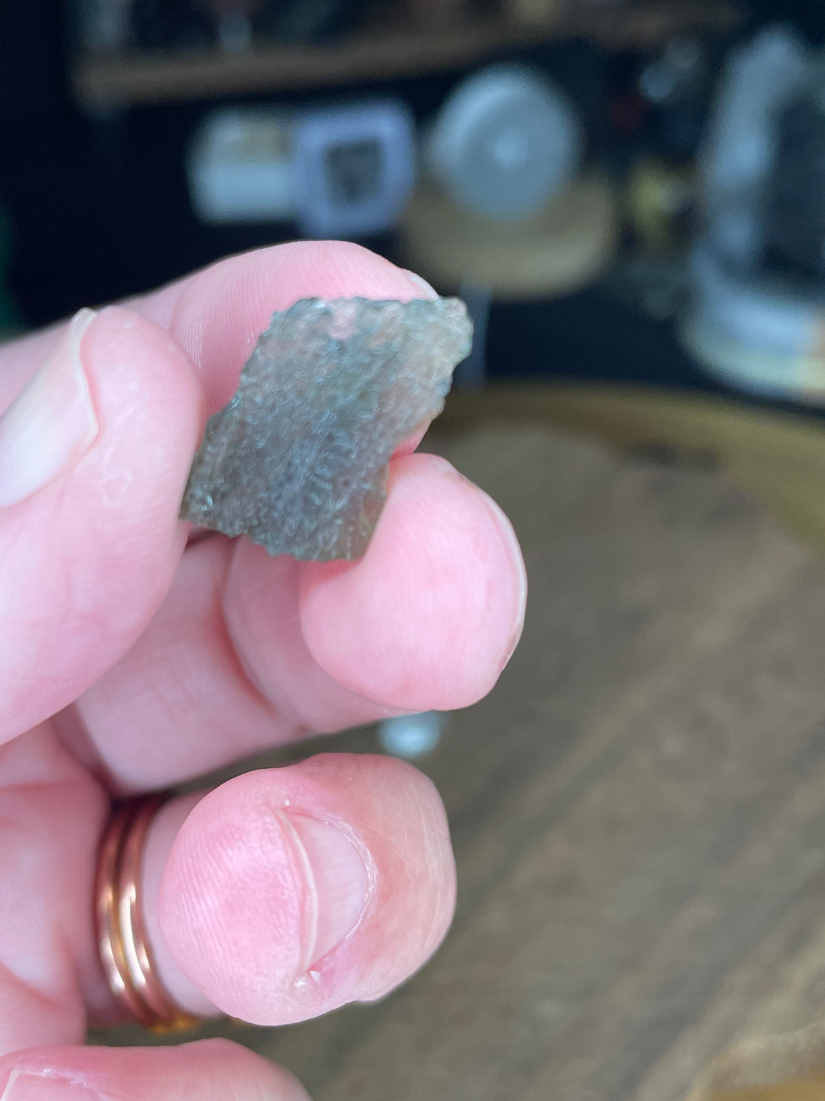 A hand holding a small, textured, translucent green Moldavite with Herkimer Diamonds - 1.15 g fragment.
