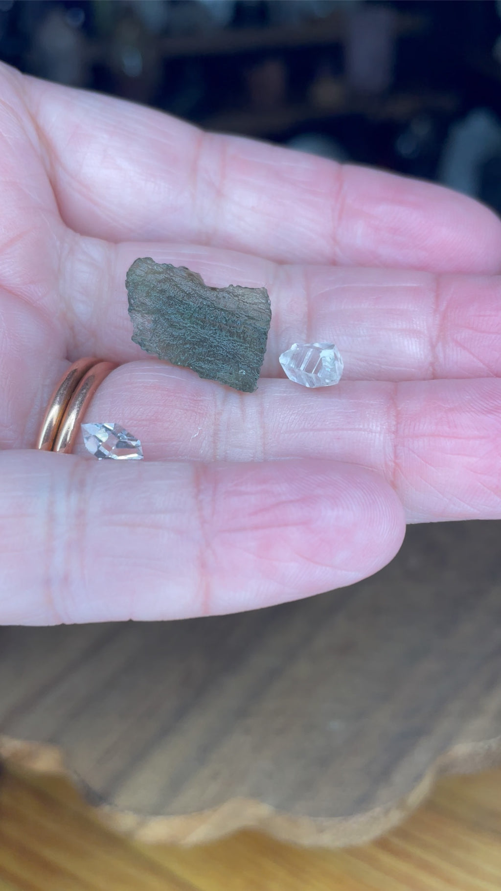 A person’s palm holding one textured, dark green Moldavite with Herkimer Diamonds - 1.15 g and two small, clear, faceted crystals.