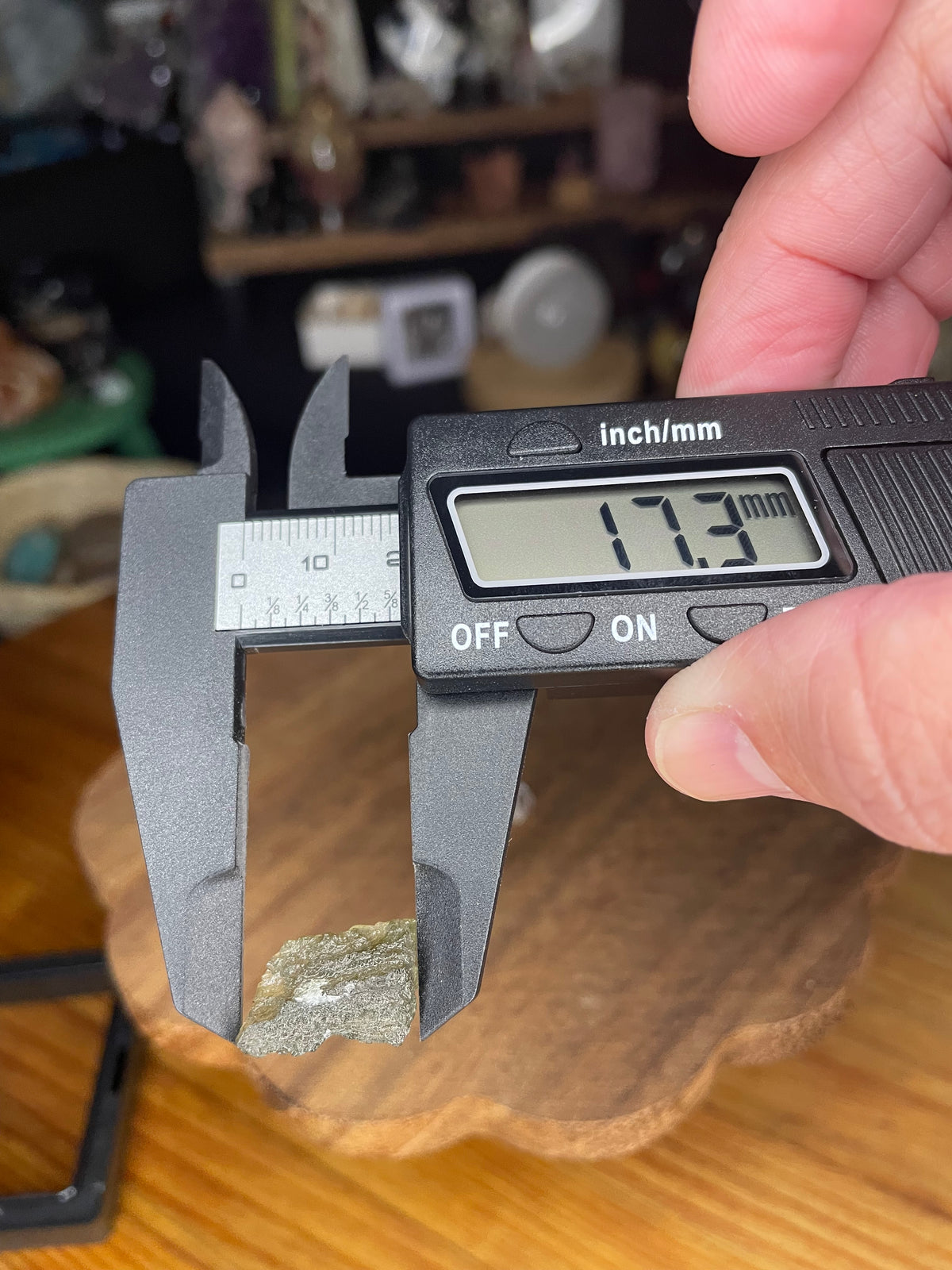 A raw, green, textured Moldavite with Herkimer Diamonds - 1.15 g crystal being measured by a digital caliper showing 17.3 mm.
