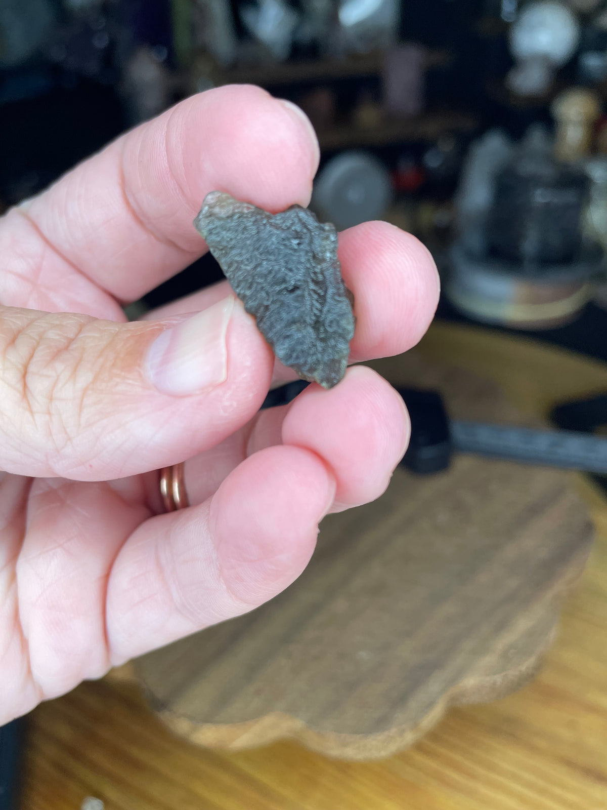 A hand holding a small, textured, dark green Moldavite with Herkimer Diamonds - 2.37 g mineral fragment.