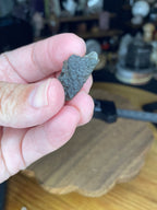 A hand holds a small, textured, olive-green Moldavite with Herkimer Diamonds - 2.37 g.