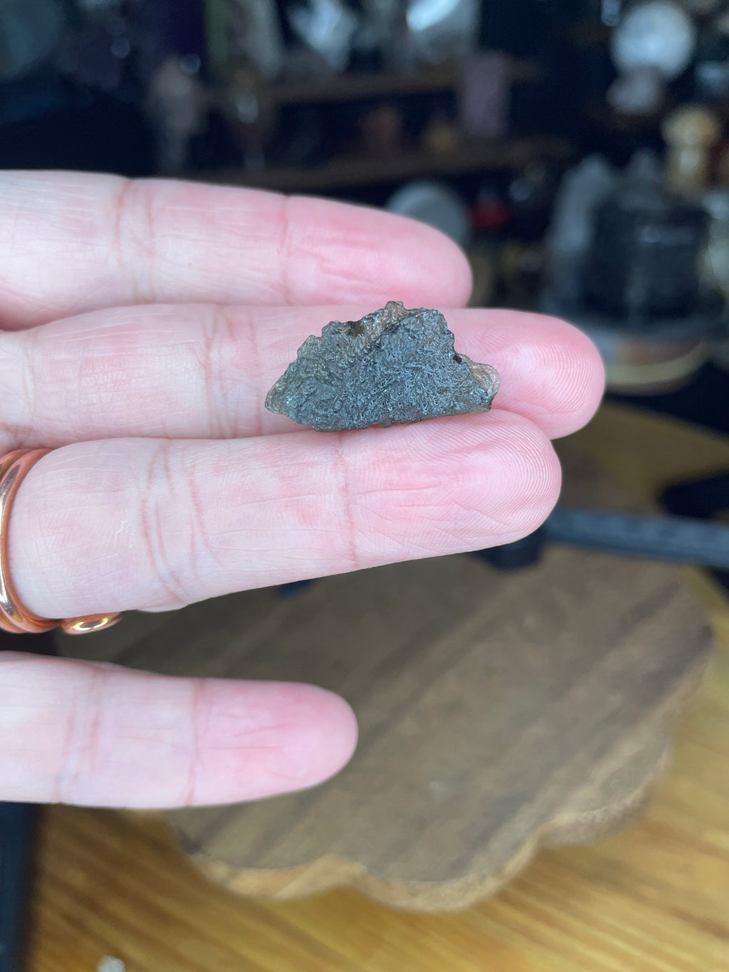A small, dark, textured piece of Moldavite with Herkimer Diamonds - 2.37 g held between two fingers.