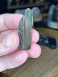 A hand holds a translucent, olive-green piece of textured Moldavite with Herkimer Diamonds - 3.4 g.
