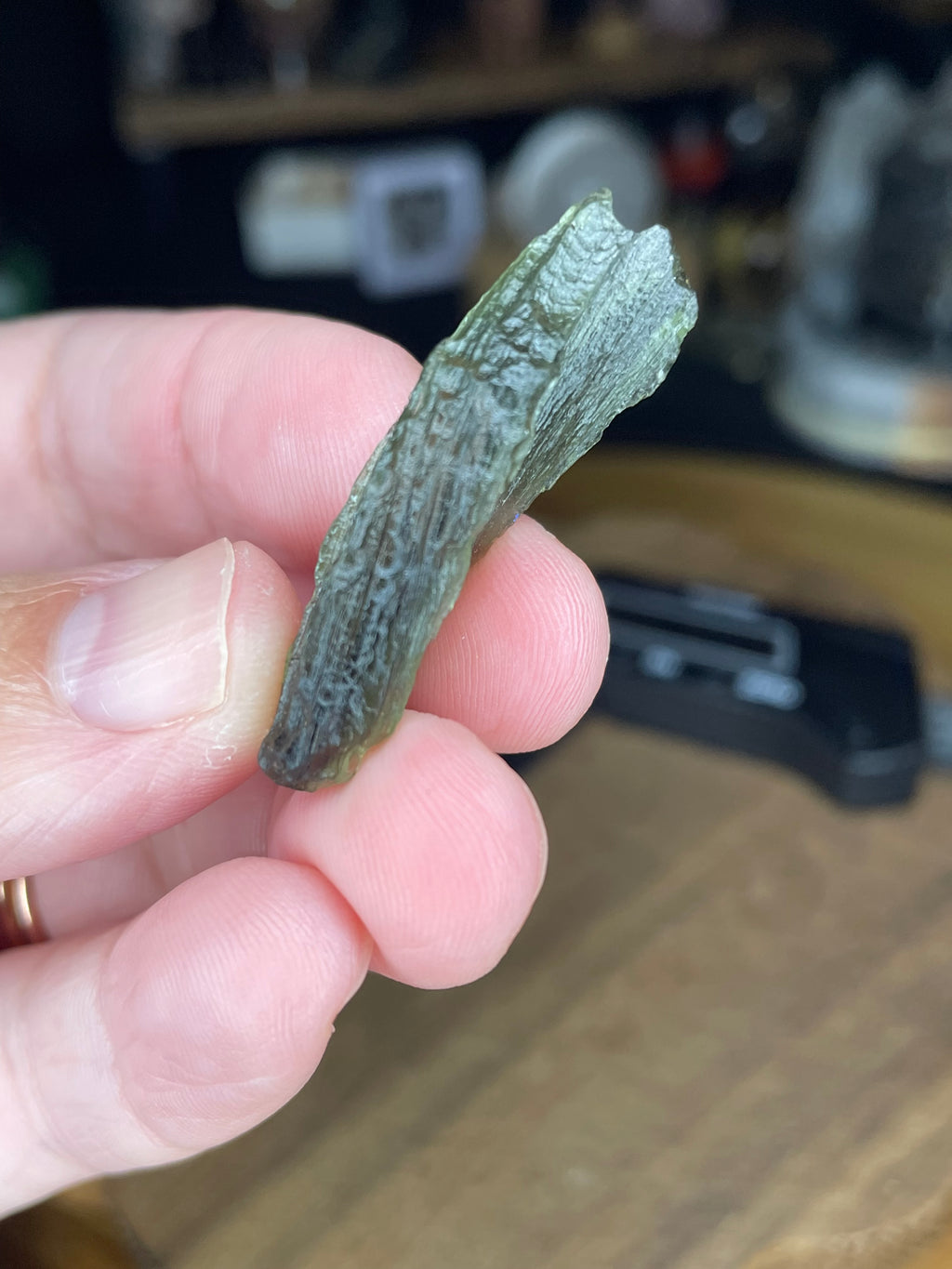 A hand holds a textured, olive-green Moldavite with Herkimer Diamonds - 3.4 g.