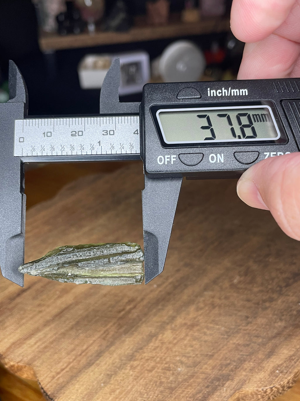 A piece of green, textured Moldavite with Herkimer Diamonds - 3.4 g held in digital calipers measuring 37.8 millimeters.