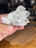 A hand holds a 108 g Apophyllite Specimen cluster of clear, geometric crystals.