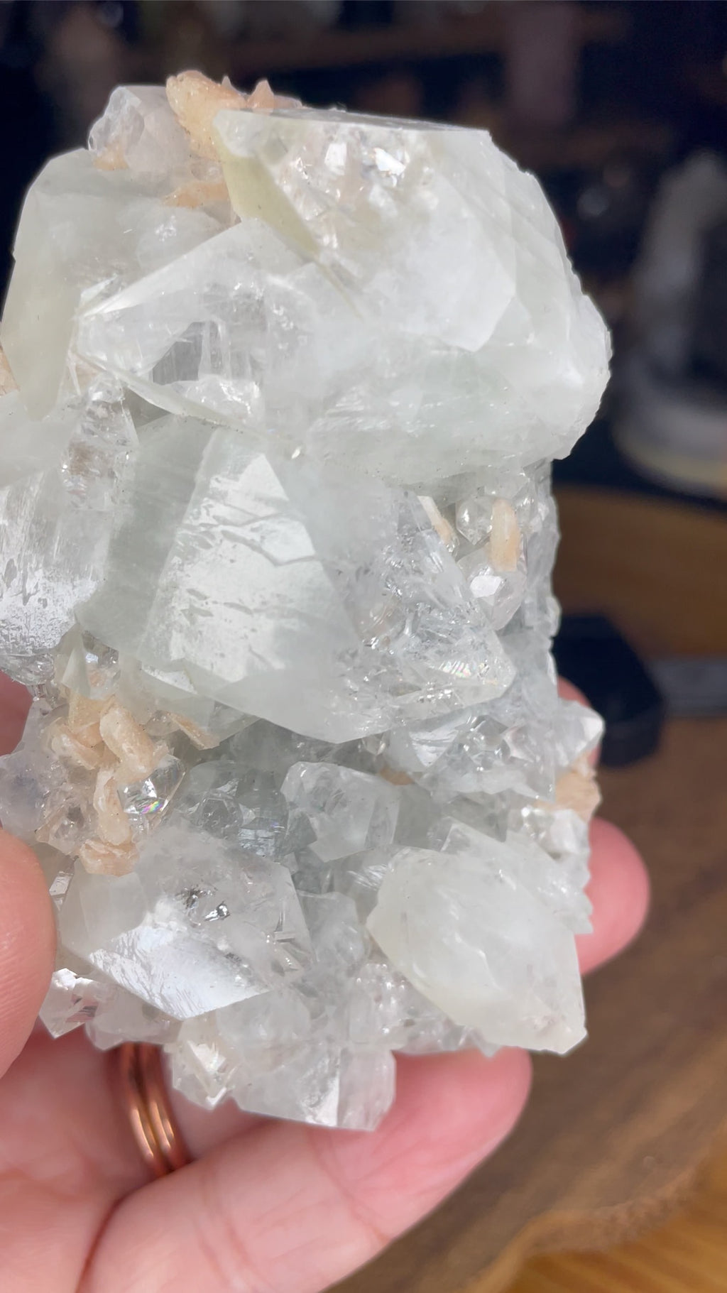 A hand holds a 178 g cluster of translucent, blocky Apophyllite with Stilbite crystals accented with small peachy-pink mineral deposits.