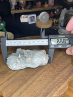 A 178 g Apophyllite with Stilbite specimen consisting of clear apophyllite crystals with peach-colored stilbite, shown being measured by digital calipers at 88.8 millimeters.