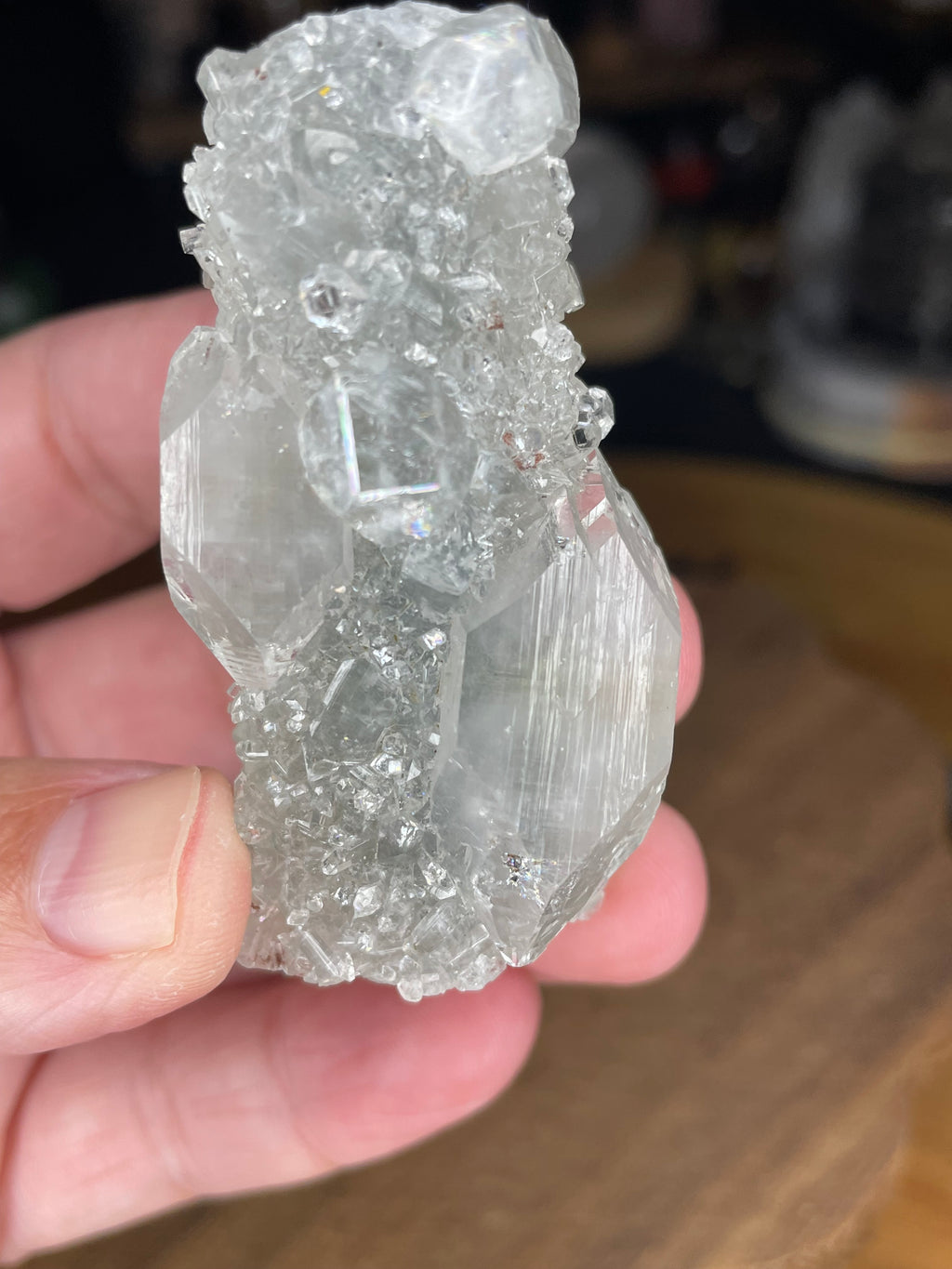 A hand holding an Apophyllite with Black Chalcedony - 50 g cluster featuring clear, crystalline, and faceted surfaces.