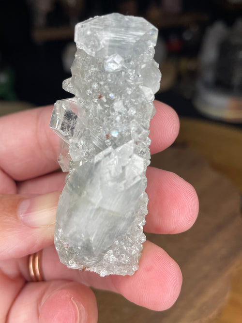 Hand holding an Apophyllite with Black Chalcedony - 50 g specimen, a translucent, crystalline mineral with a textured surface and defined, clear geometric points.