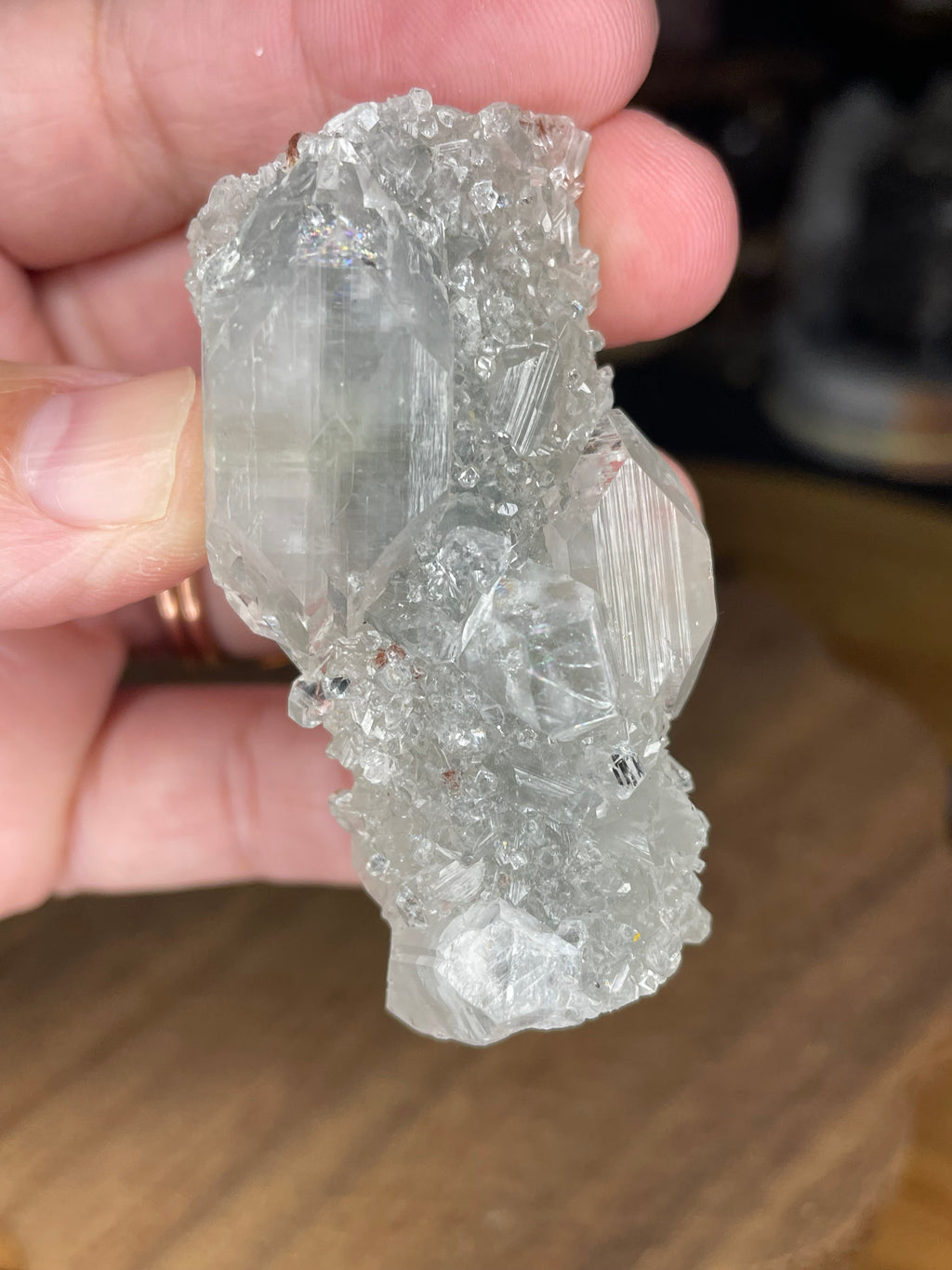 A hand holds a 50 g Apophyllite with Black Chalcedony cluster of clear, geometric crystals with dark chalcedony at the base.