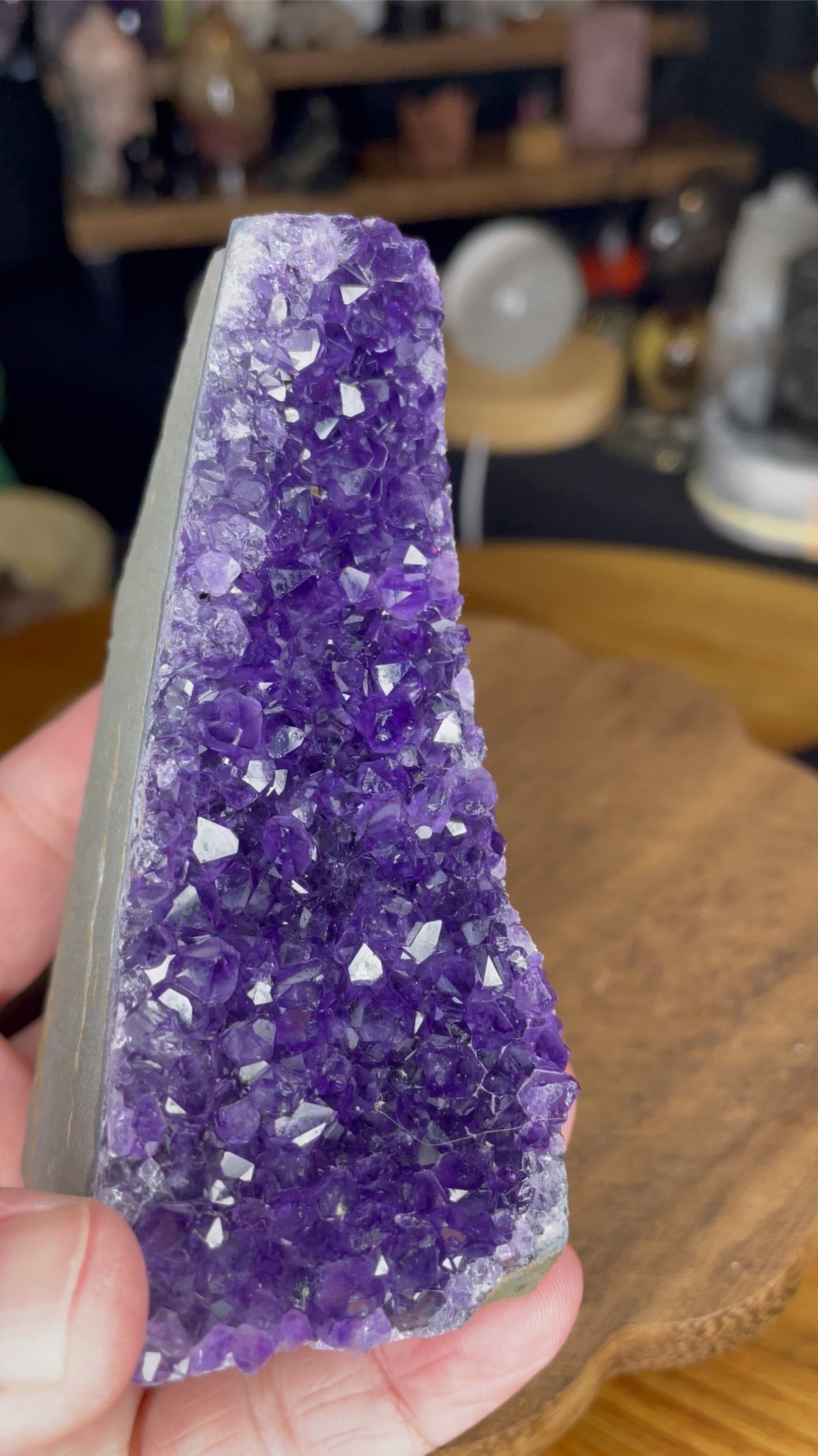A hand holds a triangular Brazilian Amethyst Cut Base - 304 g, featuring a purple crystal with a flat, cut base.