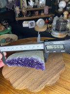 A Brazilian Amethyst Cut Base - 304 g raw geode slice with a flat bottom being measured by a digital caliper showing 99.9 millimeters.
