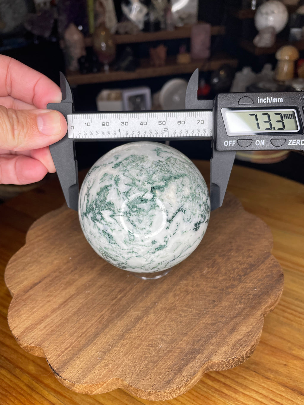 A Sirius and the Wren Tree Agate Sphere with Druzy being measured by a digital caliper showing 73.3 mm.
