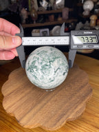 A Sirius and the Wren Tree Agate Sphere with Druzy being measured by a digital caliper showing 73.3 mm.