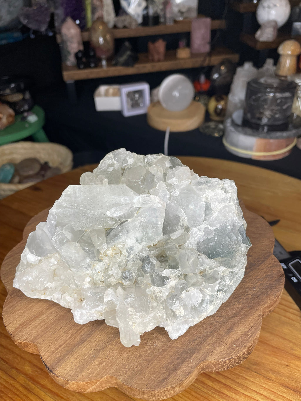 A raw, translucent Brazilian Blue Tara Quartz Cluster - 600 g with pale blue-tinted points resting on a flower-shaped wooden base.