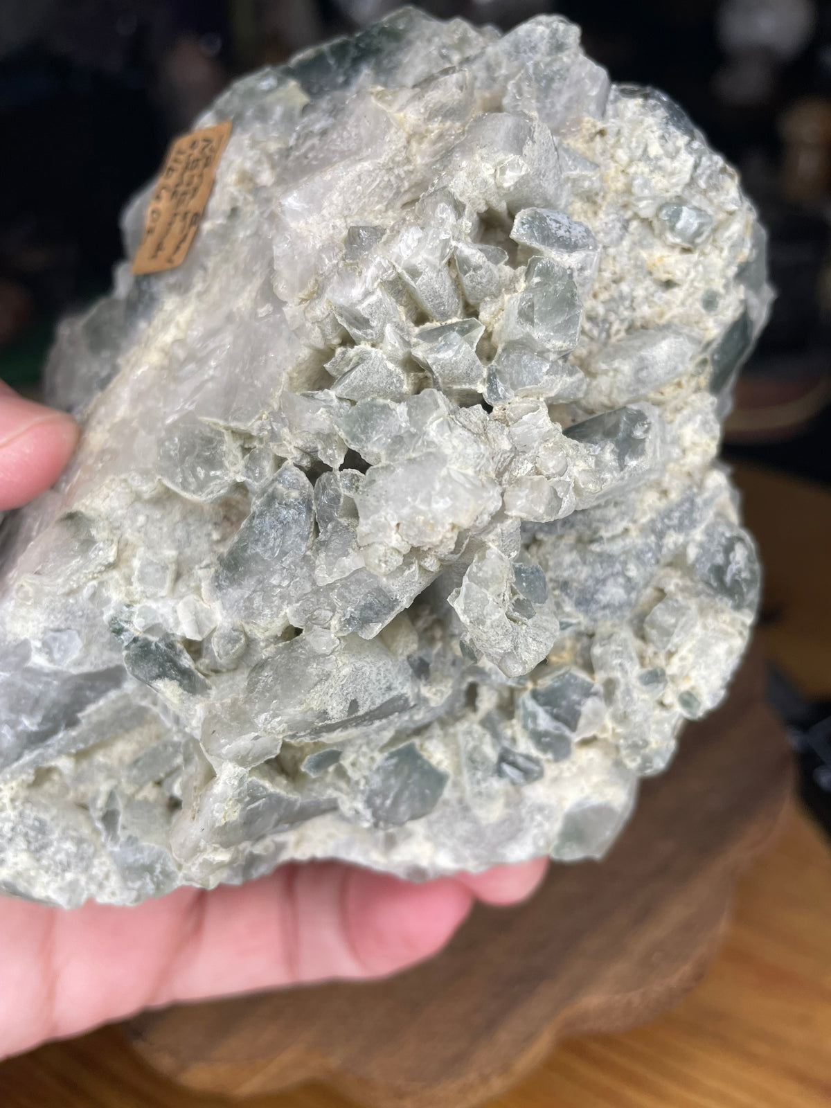 A hand holds a Brazilian Blue Tara Quartz Cluster - 600 g, featuring a jagged cluster of translucent, pale blue and white crystals.