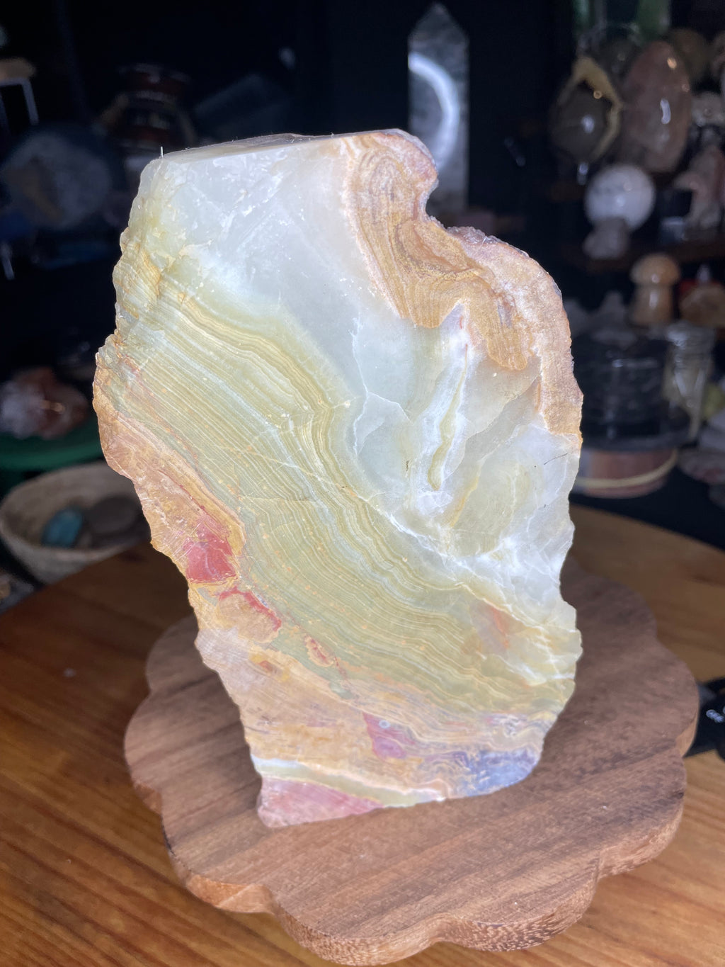 Large Green Banded Calcite (Green Onyx) Specimen featuring an irregularly shaped piece of banded mineral with layers of green, cream, tan, and reddish-brown, standing on a wooden base.