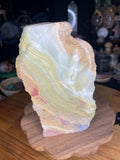 Large Green Banded Calcite (Green Onyx) Specimen featuring an irregularly shaped piece of banded mineral with layers of green, cream, tan, and reddish-brown, standing on a wooden base.