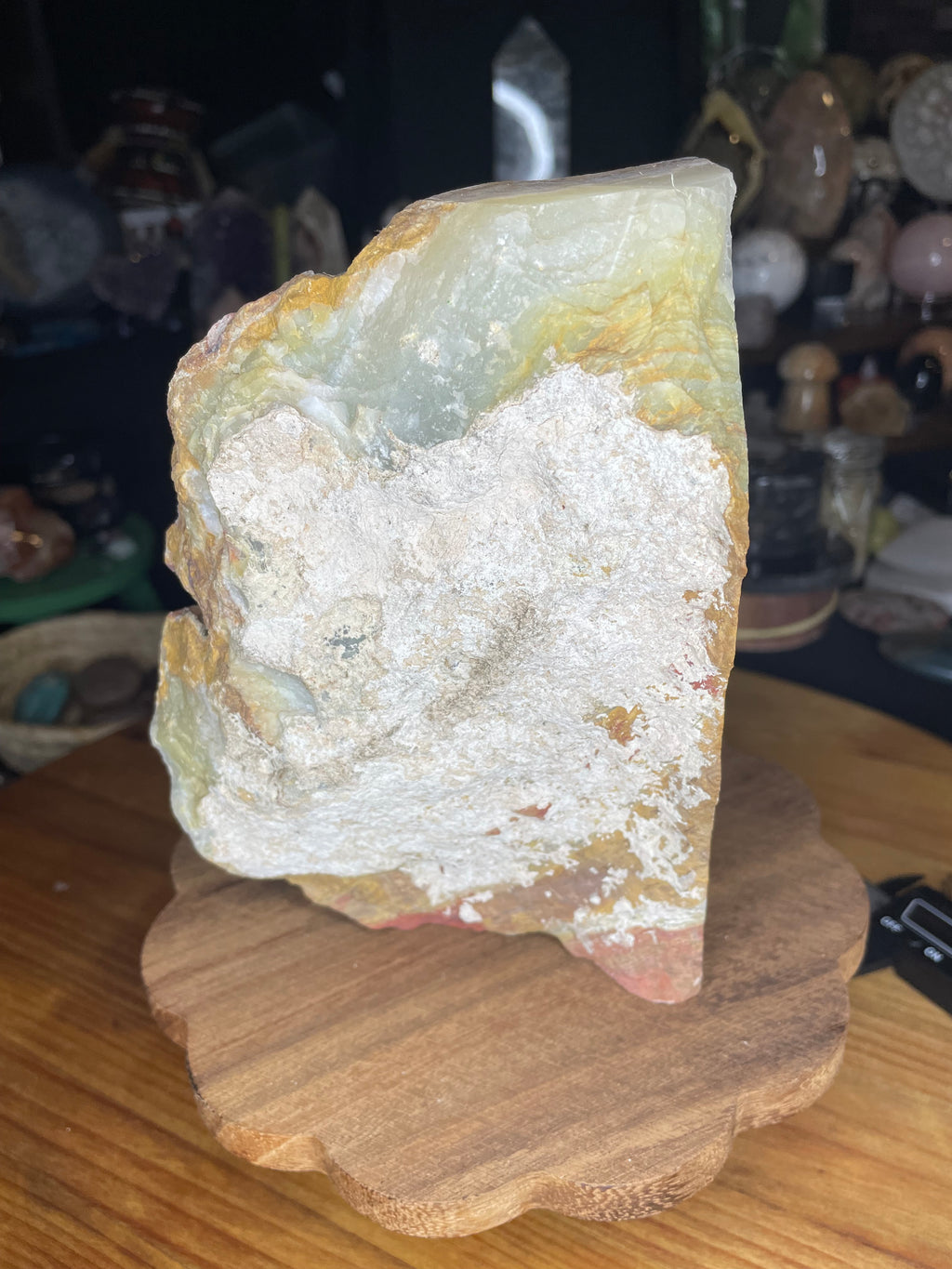 Large, rough Large Green Banded Calcite (Green Onyx) Specimen with green and orange banding resting on a wooden base.