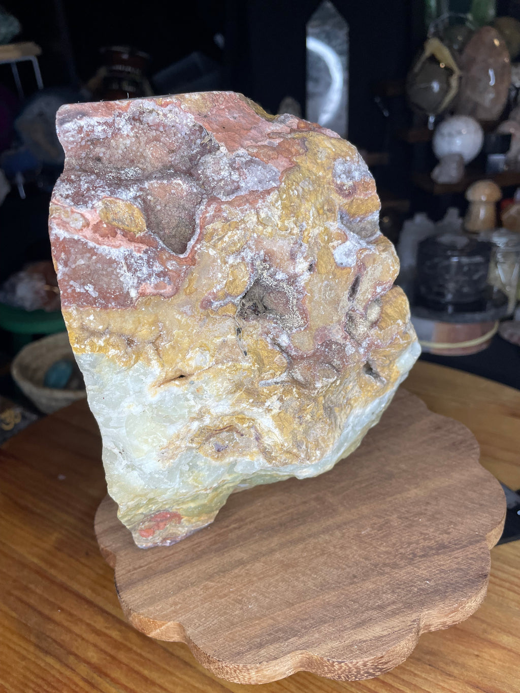 A large, rough-cut specimen of Large Green Banded Calcite (Green Onyx) in shades of cream, yellow, and rusty red, displayed on a wooden stand.