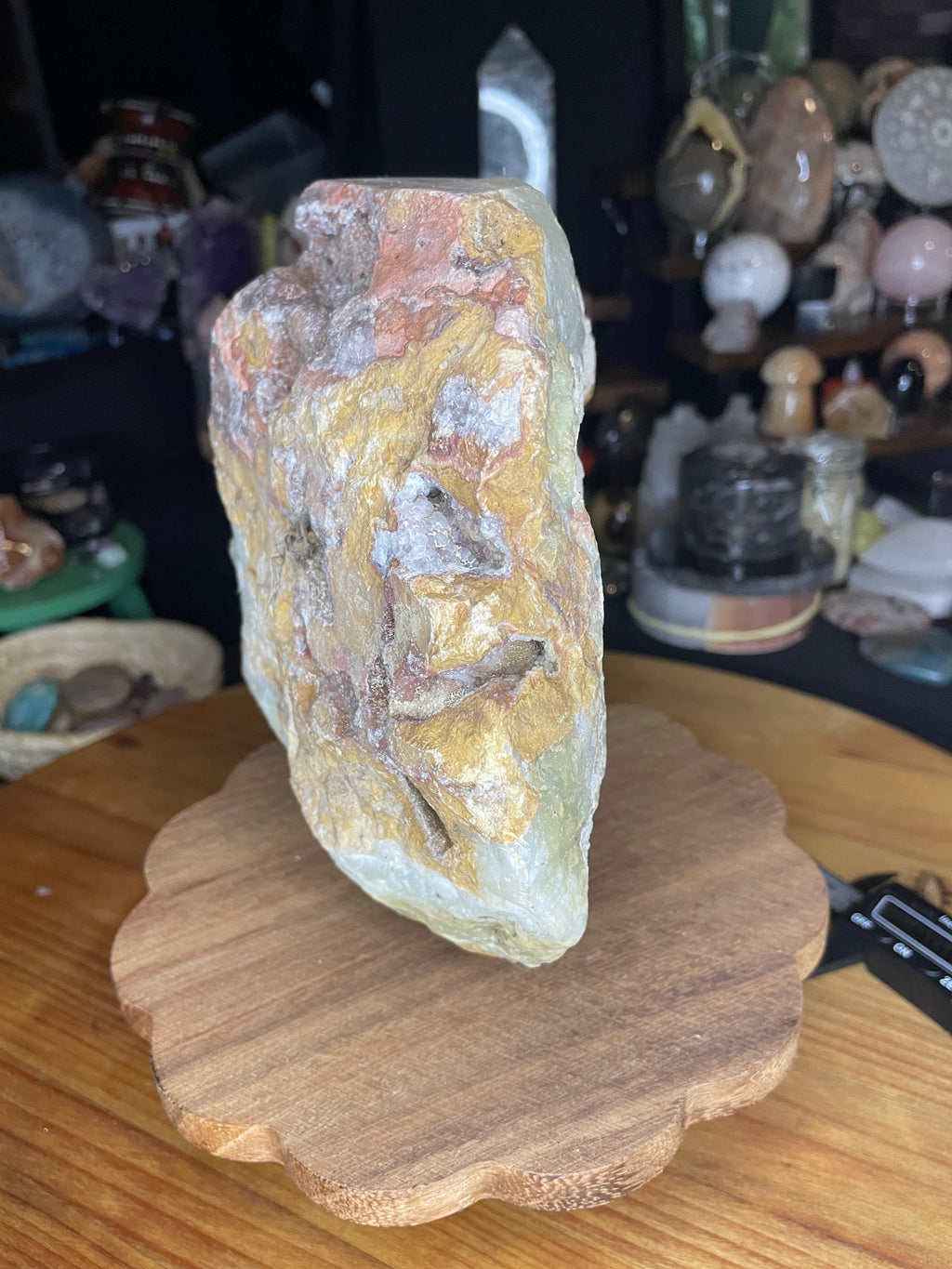 A Large Green Banded Calcite (Green Onyx) Specimen consisting of a thick slab of banded green and tan calcite resting upright on a wooden scalloped display stand.