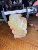 Digital calipers measure the width of a Large Green Banded Calcite (Green Onyx) Specimen at 91.8 millimeters, revealing its banded green and tan stone surface.