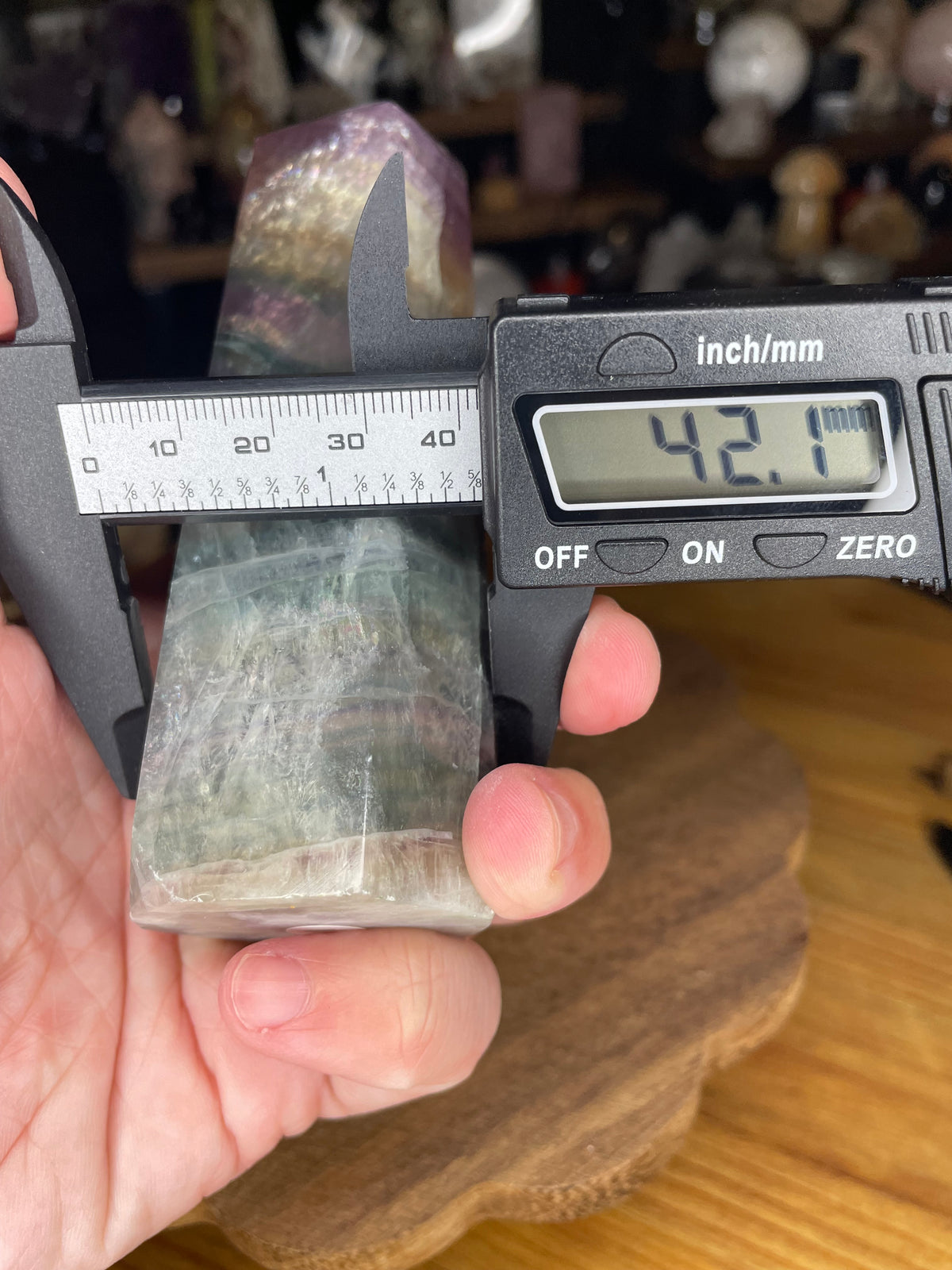 A hand holds a digital caliper measuring the width of a Chunky Rainbow Fluorite Tower, with the display reading 42.1 mm.