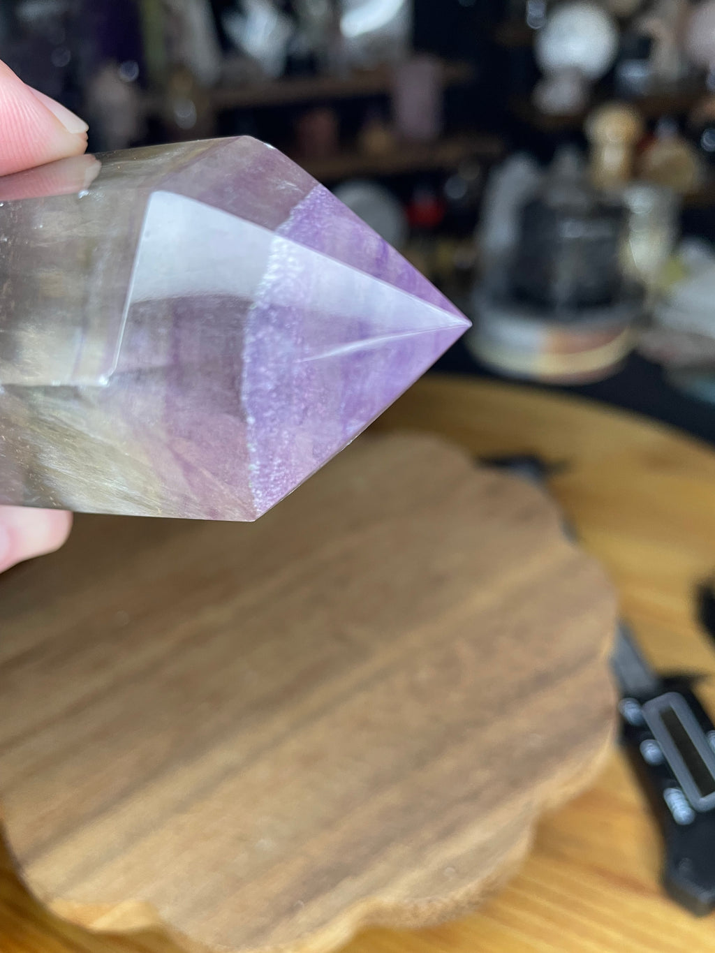 A hand holding a 428 g Chunky Rainbow Fluorite Tower - UV Reactive - from Sirius and the Wren, featuring a polished crystal with distinct purple and clear layers.