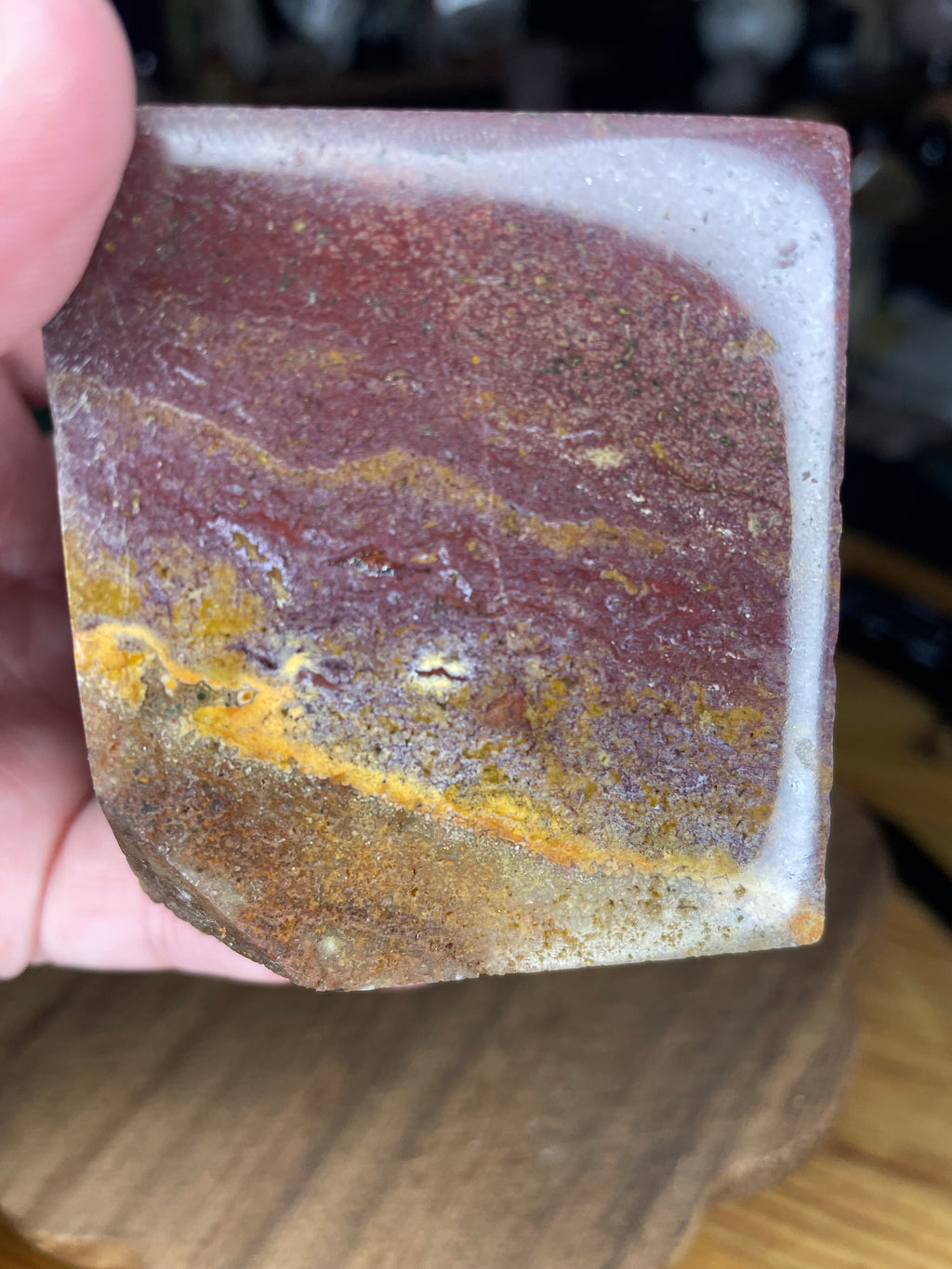 A hand holding an Ocean Jasper Floating Cube - 18.5 oz, a polished reddish-brown jasper cube with layers of yellow and white banding.