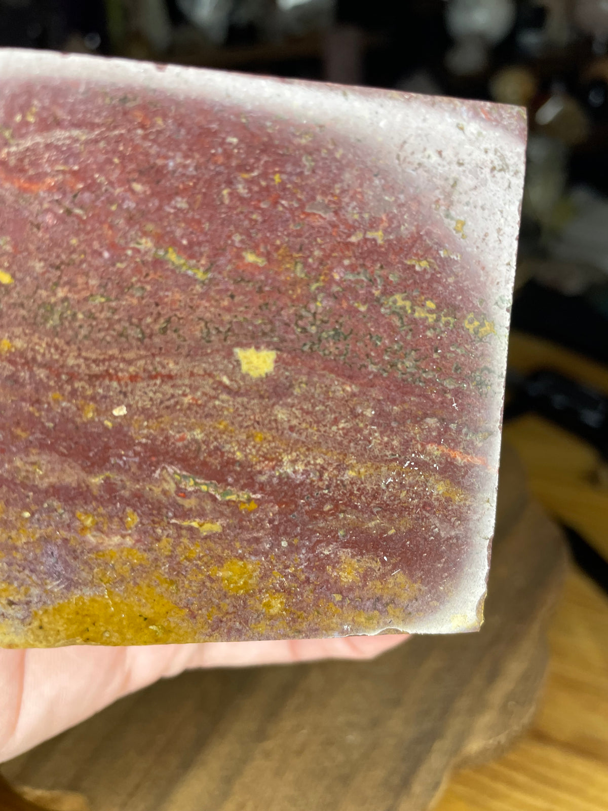 A close-up view of an Ocean Jasper Floating Cube - 18.5 oz, a polished cubic stone featuring mottled patterns of deep red, brown, and yellow.