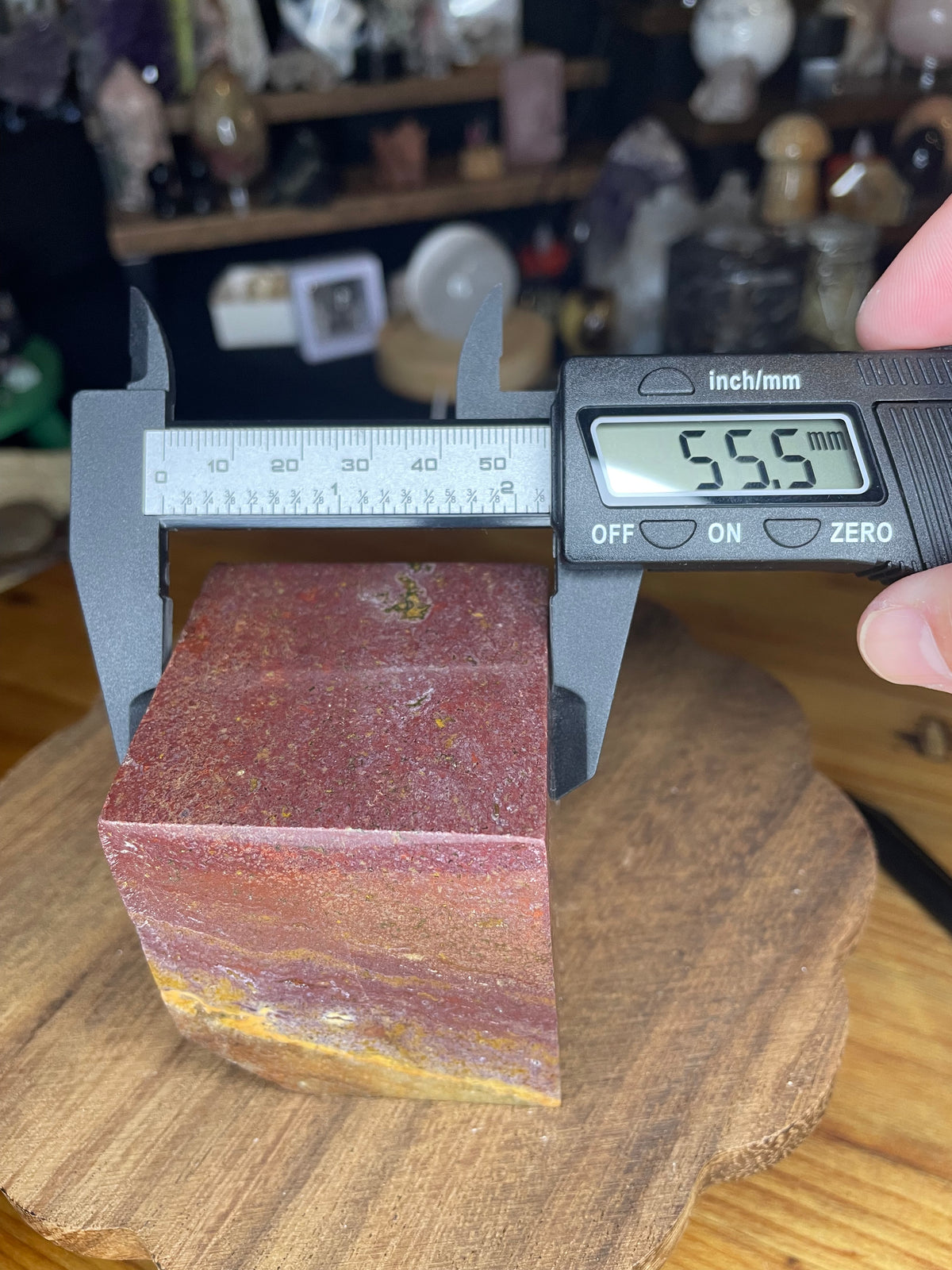 A red and yellow Ocean Jasper Floating Cube - 18.5 oz being measured by digital calipers, which display a reading of 55.5 mm.