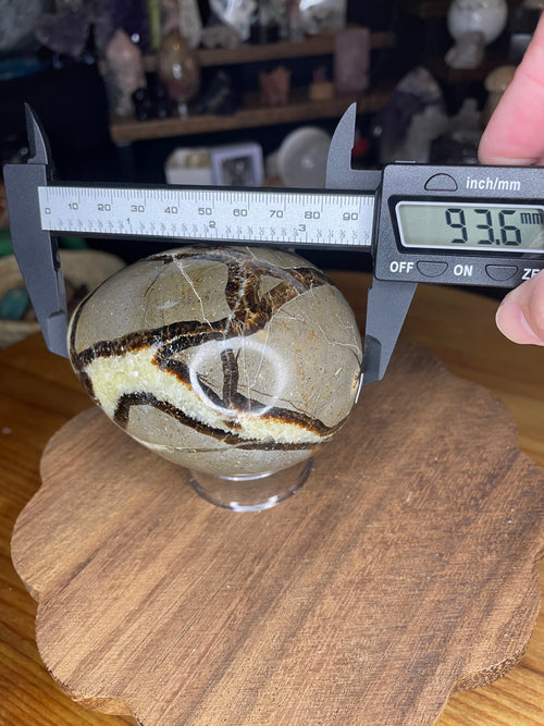 A smooth, oval-shaped Big Mama Septarian Egg - UV Reactive - 22.9 oz being measured by a digital caliper, which displays 93.6 mm.