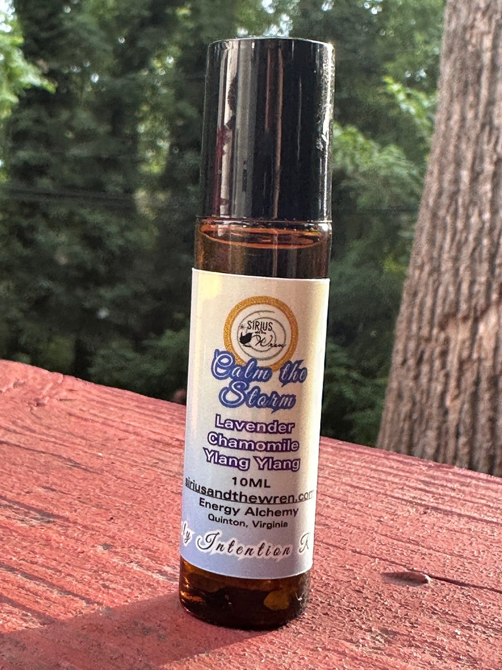 Calm the Storm Intention Roller on a wooden surface with trees in the background